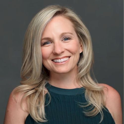 A person with blonde hair and a teal top is smiling against a neutral background.
